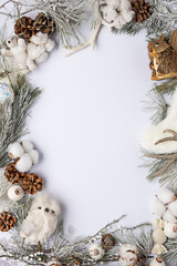 Christmas decorative border frame made with pine tree branch, owl, cotton flower and pine cone on bright background. Minimal New Year mock up concept. Flat lay.