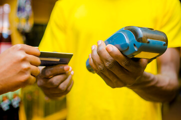 cropped image of man wearing a yellow t-shirt, holding a pos terminal and collecting a credit for withdraw.