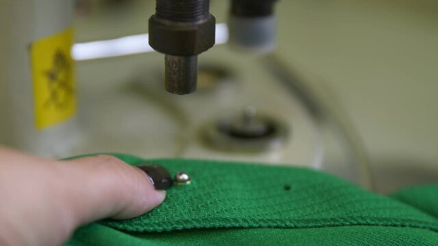Seamstress installs metal eyelets into green hockey uniform