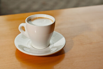 White coffee cup on a wooden board. Blurred bar interior on background. Free space near the coffee.