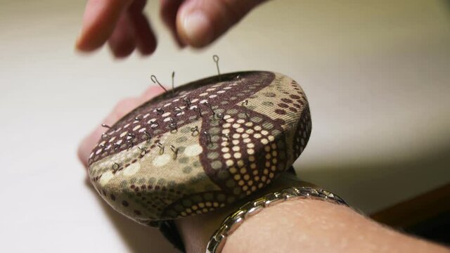 Seamstress takes and puts pin into cushion on wrist closeup