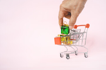 Fototapeta premium human's hand holding green small gift box in shopping cart on sweet pink background