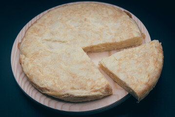 Tortilla de patata cortada en una plato de madera sobre fondo negro. 