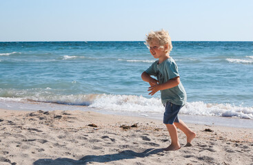 Little boy walking and playing alone on the beach. Summertime, vacation, travel, nature concept.