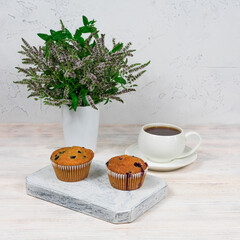 Cupcakes with black currants on a white wooden cutting board against the background of a cup of tea.
