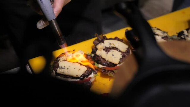Chef using blow torch to melt cheese on burger. live burger cooking process in the restaurant. 