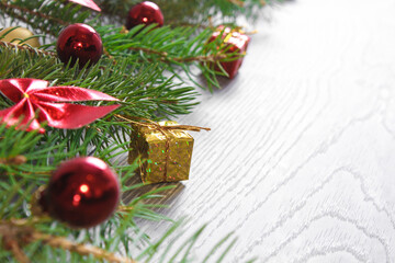 Christmas card - green tree branches with gold giftboxes, red balls and baws isolated on white wooden background.