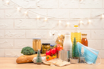 Christmas donation box - food donations on light background with copyspace - pasta, fresh vegatables, canned food, baguette, cooking oil with Christmas decorations. Food bank. Selective focus