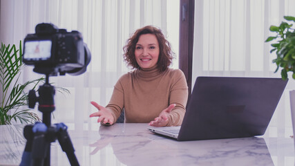 Smiling woman recording her video blog. Woman blogger videotapes her vlog at home.  Adult woman...