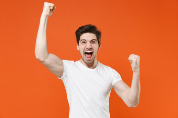 Happy joyful screaming young man 20s in basic casual white blank t-shirt standing clenching fists...