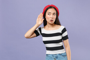 Fototapeta premium Curious shocked young asian woman 20s wearing striped t-shirt red beret standing try to hear you overhear listening intently looking aside isolated on pastel violet colour background studio portrait.