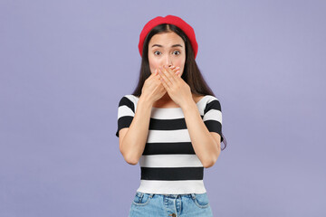 Shocked amazed worried young brunette asian woman 20s wearing striped t-shirt red beret standing covering mouth with hands looking camera isolated on pastel violet colour background studio portrait.