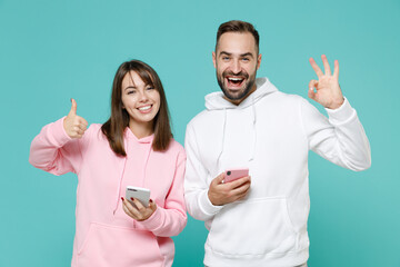 Funny young couple two friends man woman 20s in white pink casual hoodie using mobile cell phone...
