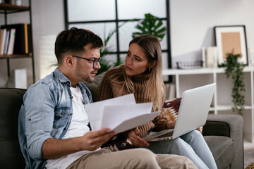 Worried couple paying their bills online with laptop at home in the living room. Couple having financial problems.