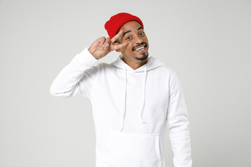 Smiling cheerful young african american man 20s years old wearing casual basic streetwear hoodie standing covering mouth with hands looking camera isolated on white colour background studio portrait.