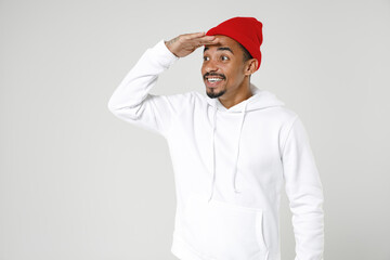 Smiling young african american man 20s years old wearing casual basic streetwear hoodie standing holding hand at forehead looking far away distance isolated on white colour background studio portrait.
