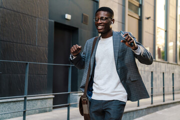 Happy african american man using mobile phone while dancing on street