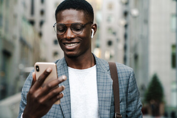 Happy african american man in earphones using mobile phone