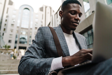 African american man working with laptop while sitting on staircase