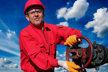 Oil Field Worker Turning Valve On Oil Rig - Portrait of a Worker Against Blue Sky With White Clouds at Pump Jack Oil Well