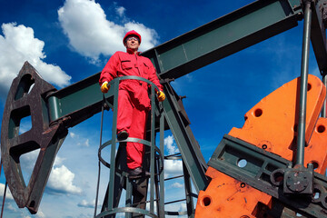 Oil Worker and Petroleum Industry Pump Jack - Worker in Red Coveralls and Protective Clothing Standing at Pump Jack Pumping Unit