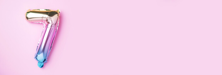 Creative layout. Rainbow foil balloon number and digit seven 7. Birthday greeting card. Anniversary concept. Top view. Copy space. Stylish colored numeral over pink background. Numerical digit.