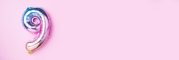 Creative layout. Rainbow foil balloon number and digit nine 9. Birthday greeting card. Anniversary concept. Top view. Copy space. Stylish colored numeral over pink background. Numerical digit.