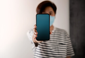Mobile Phone Mockup Image. Display Screen is Blank. Person with a Surgical Mask on Face Holding a Smartphone towards the Camera. Front View