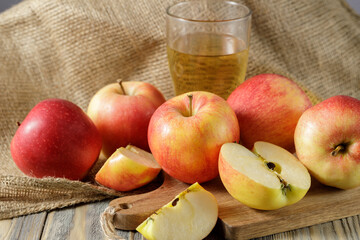 Fresh harvesting red apples and glass of cider or sparkling juice on wooden table over canvas bag.