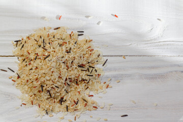 Fototapeta na wymiar A mixture of brown, wild, red, white rice lies on a slide on the wooden white surface of the table.