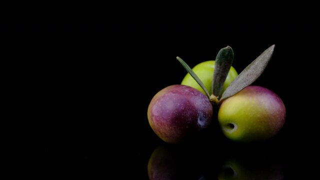 Olives. Elegance black and green olives with leaves rotating on black reflective ground.