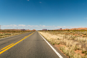 Fototapeta na wymiar An empty road going towards some mountains on the horizon and almost with no clouds. Arizona, United States