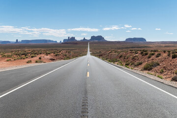 Route with a straight view to the most iconic view of Monument Valley National Park with a cloudless sky at Utah, United States. Some clouds can be seen on the horizon