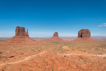 Dirty road passes by the most iconic view of Monument Valley National Park with a cloudless sky at Utah, United States.