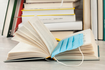 Wide open book with medical mask as bookmark and  stack of books as background.