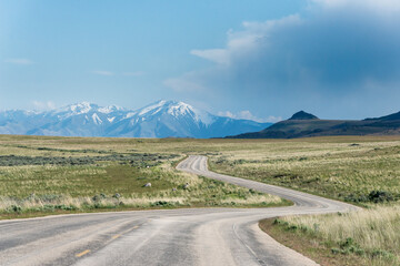 Winding road towards the snow capped mountains on the horizon with some prairies around it, at Antelope Island State Park, close to Salt Lake City, Utah