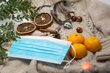 Medical mask and accessories for the New Year, a green twig, dry oranges, tangerines, a woolen sweater. Flatley on a white background.