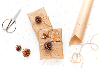 Gift box in craft paper, decorated with a pine cone on a white background, scissors and wrapping paper nearby. The concept of preparing gifts for the holiday