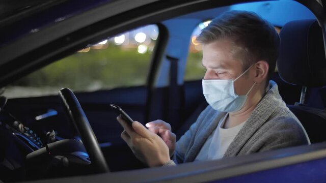Man wearing a mask sitting in car after work, talking on mobile phone with voice recognition ai audio message. Freelancer using smartphone while driving. Tired businessman overworked enterpreneur