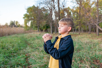 The boy clasped his hands together and offers prayer to God in the open air park.