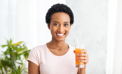 Healthy eating and detox concept. Smiling black woman with glass of fresh orange juice at home,...
