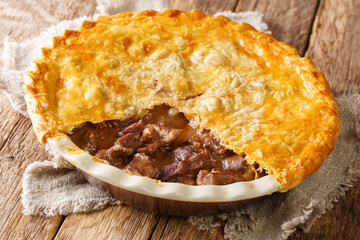 Traditional recipe of English beef steak pie with crispy puff pastry close-up in a baking dish on the table. horizontal