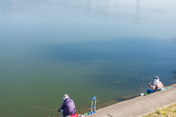 秋の公園の池で釣りをしている人