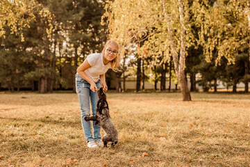 Fototapeta premium Teenager blonde girl with big glasses laughing and playing with little puppy spaniel in the warm park