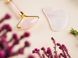 Pink quartz guasha face roller on floral background. Chinese beauty massage tool.
