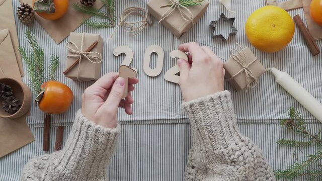 A girl lays out the wooden numbers 2021 on the table in a Christmas atmosphere, top view. Concept 2021 new year is coming. New year's natural background. Craft paper gifts with your own hands.