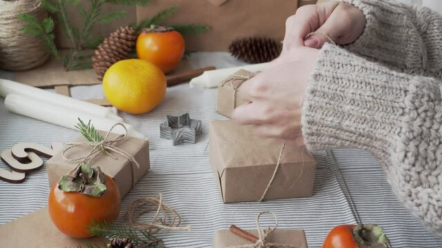 The girl packs a Christmas gift in Kraft paper, ties a bow with a rope. Gifts for new year are handmade. Christmas atmosphere, gift packer's Desk.