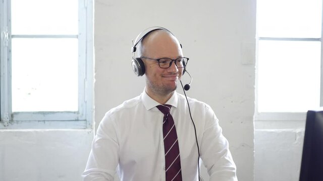 caucasian attractive worker taking a call at the office with smile. white shirt and pone computer headset. Focused businessman telemarketer telesales agent wear wireless headset make conference video 