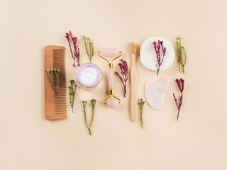 Zero waste beauty skin care reusable products framed by field flowers. Wooden comb, guasha face roller, bamboo toothbrushes and cotton pads