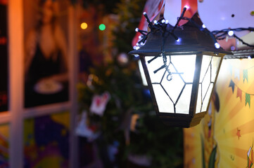 Fototapeta na wymiar christmas vintage hanging lantern with glowing lights of garlands glows on the street in the new year an night